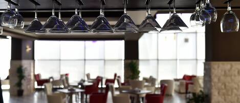 L’intérieur d’un restaurant, avec des verres à vin suspendus, des tables, des chaises et de grandes fenêtres.