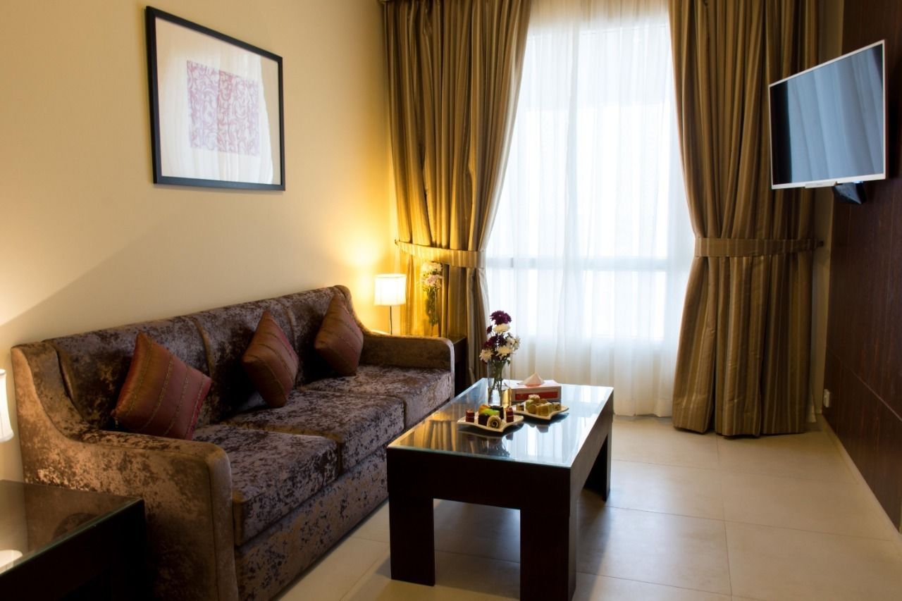 A living room with a sofa, a coffee table with snacks, a TV mounted on the wall, and curtains.