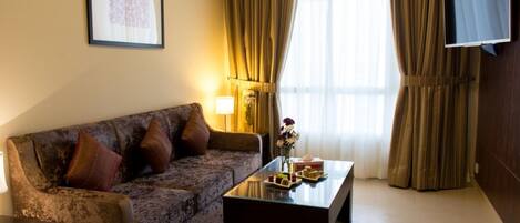 A living room with a sofa, a coffee table with snacks, a TV mounted on the wall, and curtains.