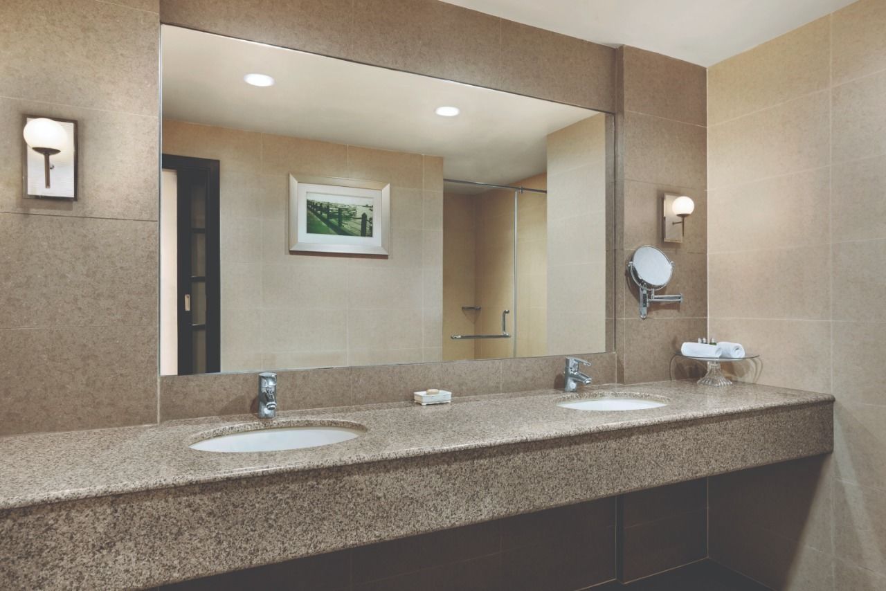 A modern bathroom with two sinks, a large mirror, and a framed picture on the wall.