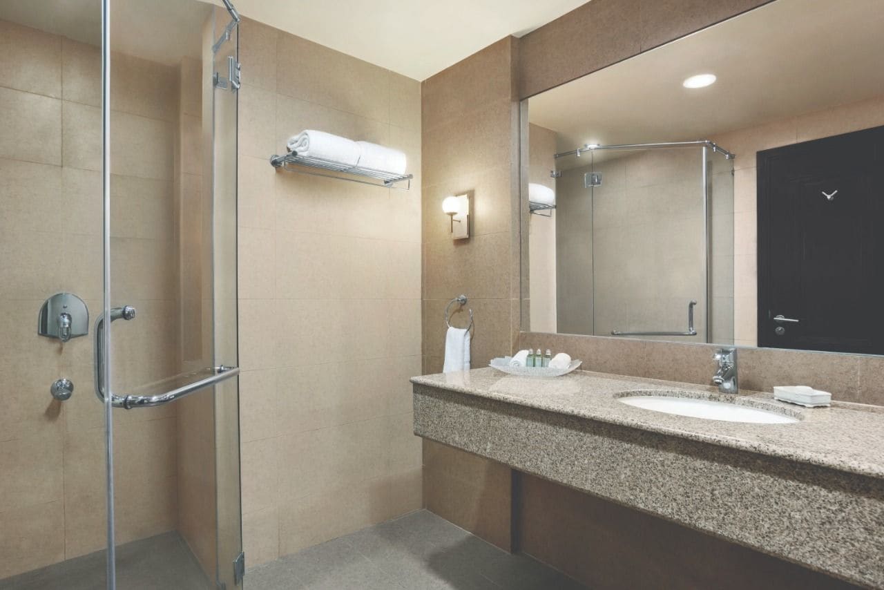 Un baño moderno con ducha envuelta en vidrio, lavamanos de granito y un espejo grande.
