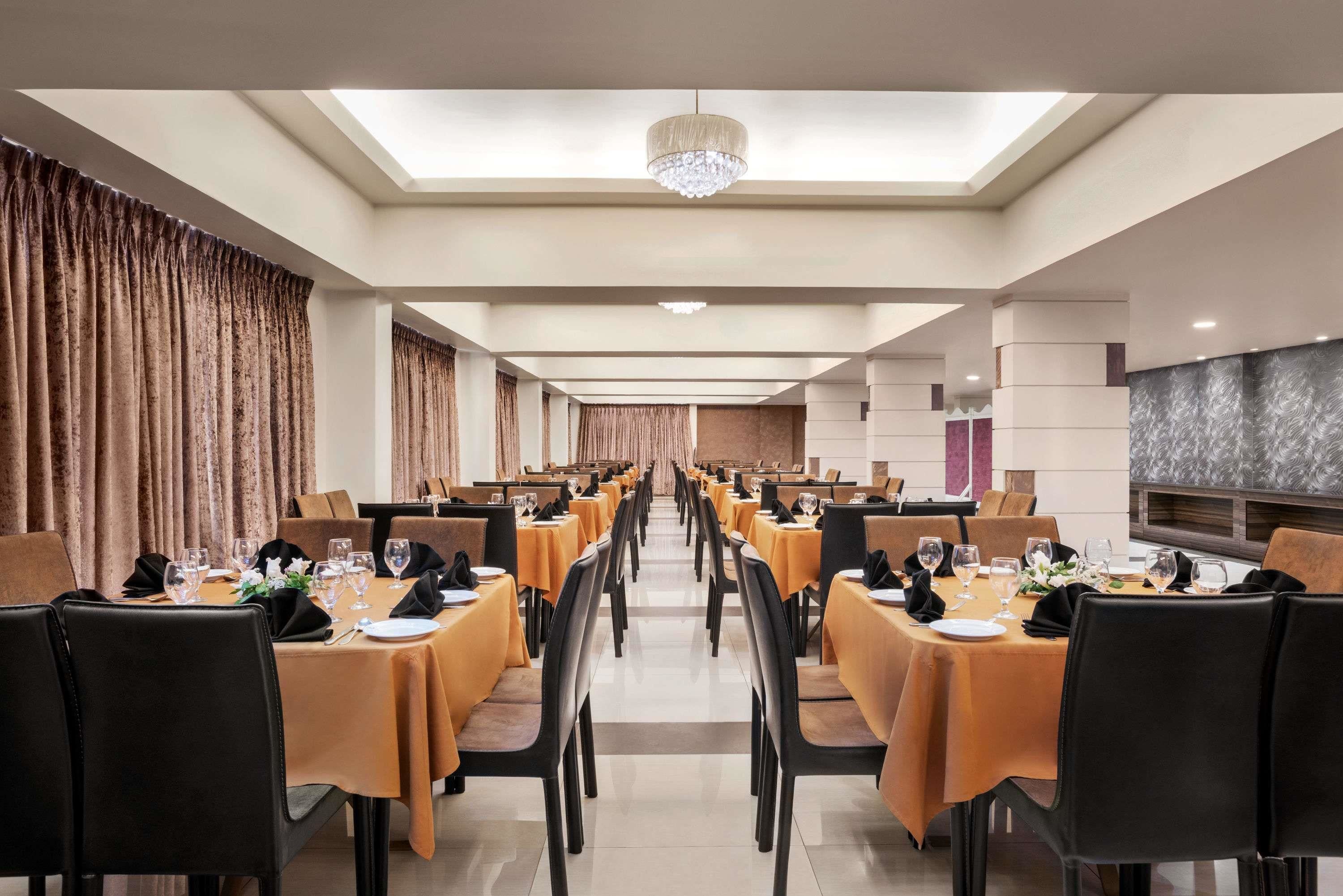 A long dining hall with tables set for a meal, featuring a chandelier and a modern design.