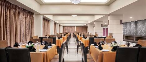 A long dining hall with tables set for a meal, featuring a chandelier and a modern design.