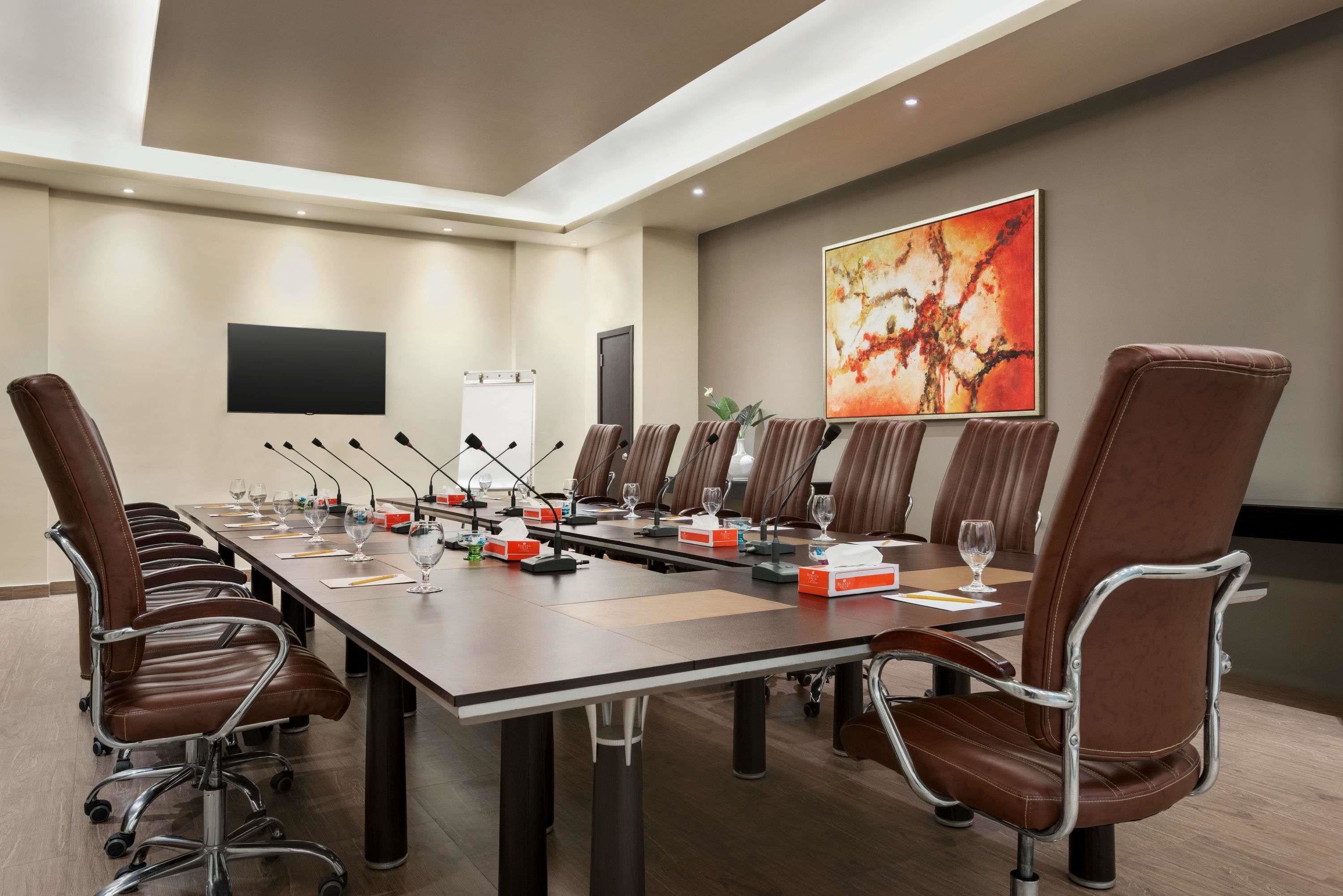 Une salle de conférence avec une longue table, des fauteuils en cuir marron, des microphones et un tableau blanc.