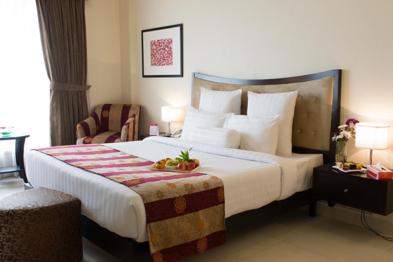 A hotel room with a large bed, a chair, a nightstand, a lamp, and a framed picture on the wall.