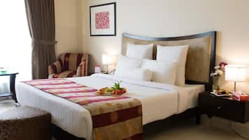 A hotel room with a large bed, a chair, a nightstand, a lamp, and a framed picture on the wall.