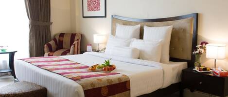 A hotel room with a large bed, a chair, a nightstand, a lamp, and a framed picture on the wall.