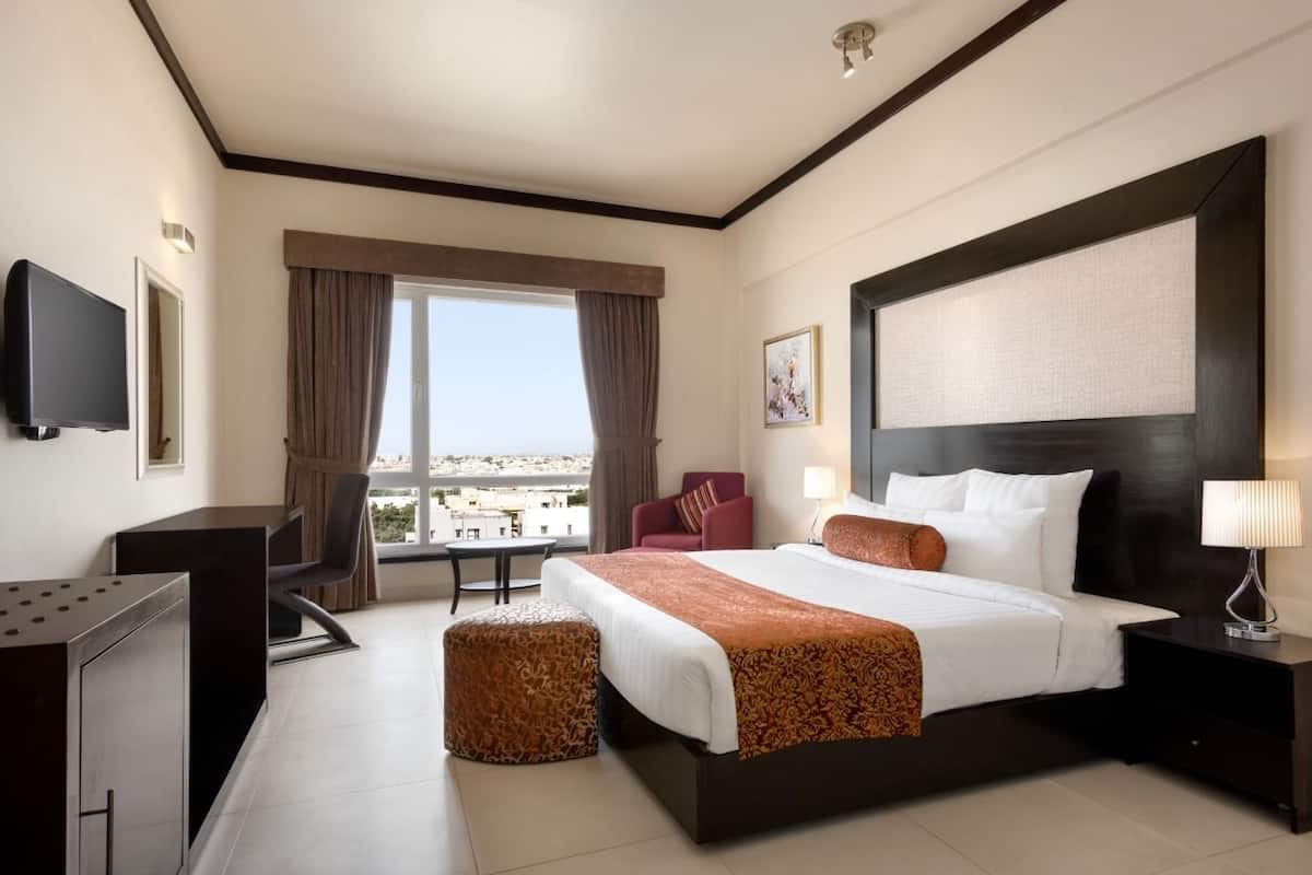 Habitación de hotel con una cama grande, un escritorio, una silla, un televisor y una ventana con vista a la ciudad.