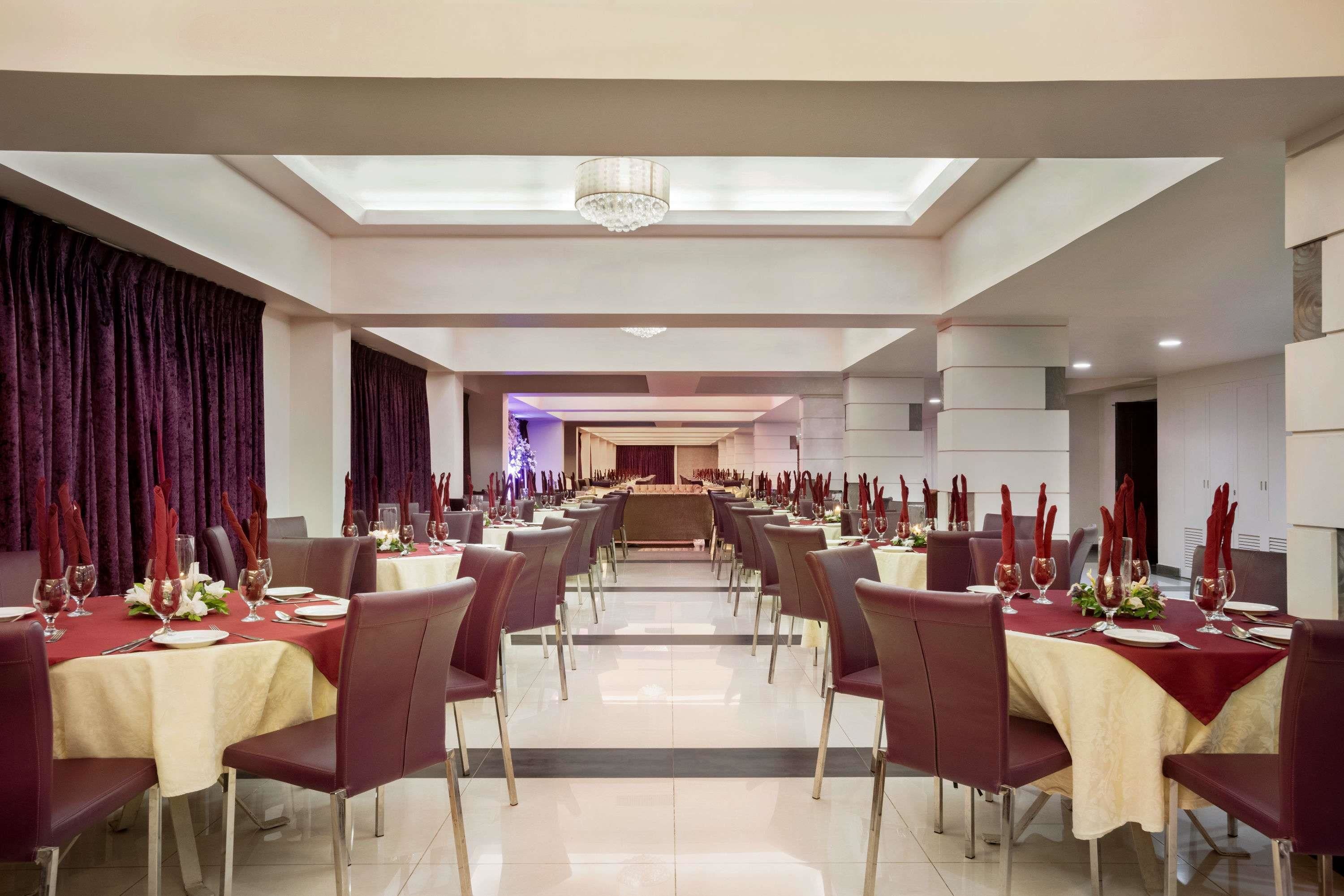 Un comedor amplio con varias mesas, cada una con servilletas rojas, manteles blancos y cubiertos.