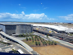 Una moderna terminal aeroportuaria con una estructura de estacionamiento de varios niveles, un puente peatonal y una zona ajardinada con árboles.