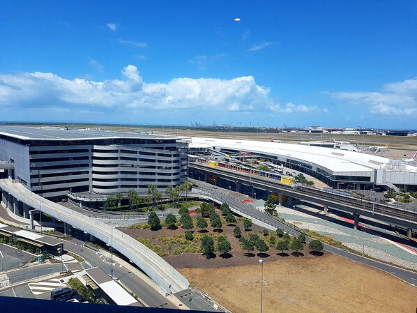 Um terminal de aeroporto moderno com uma estrutura de estacionamento em vários níveis, uma passarela e uma área ajardinada com árvores.