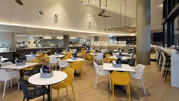 A modern restaurant with round tables and chairs, ceiling fans, and a bar area.