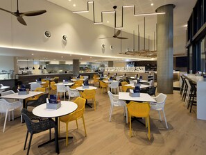 A modern restaurant with round tables and chairs, ceiling fans, and a bar area.