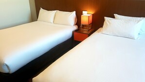Two single beds with white linens, a nightstand with a lamp between them, and a wooden headboard.