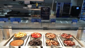 Un bufé con diversas opciones de comida, incluyendo frijoles horneados, champiñones, tocino y salchichas.
