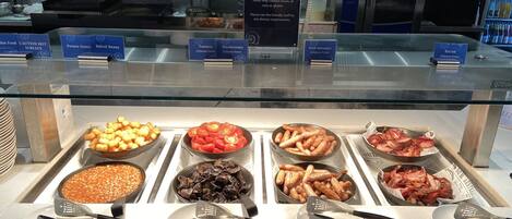 Un bufé con diversas opciones de comida, incluyendo frijoles horneados, champiñones, tocino y salchichas.