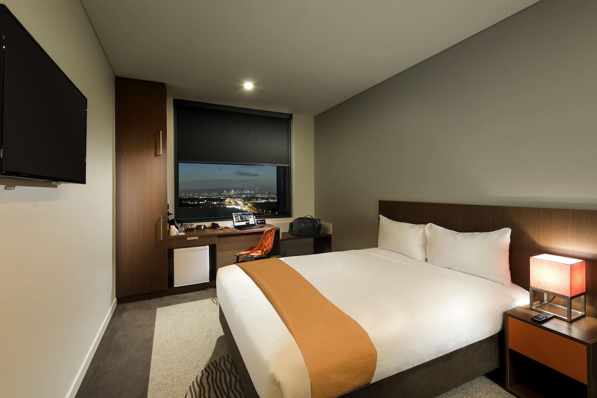 Hotelkamer met een groot bed, een bureau met een computer, een televisie en uitzicht op een stadsbeeld 's nachts.