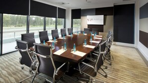 Un salón de conferencias con una gran mesa, sillas, botellas de agua y una pantalla para presentaciones.