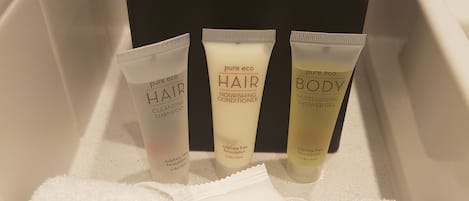 A bathroom with a black tissue box, three toiletry items (hair, hair, and body), and two white towels.