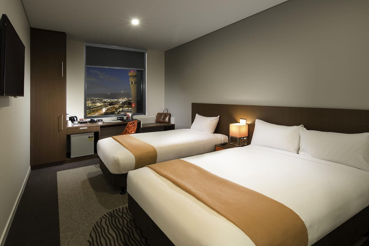 Hotelkamer met twee bedden, een bureau, een stoel, een nachtkastje met lamp en een raam met uitzicht op de stad.