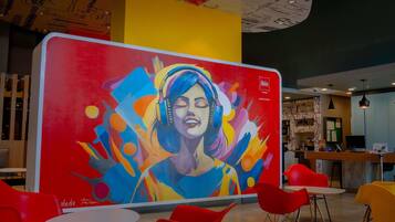 A vibrant mural with abstract art and a logo, a modern interior with red chairs and tables, and a ceiling with a unique design.