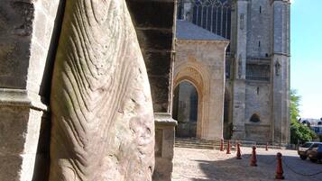 A stone sculpture, a cobblestone street, and a church with a clock tower.
