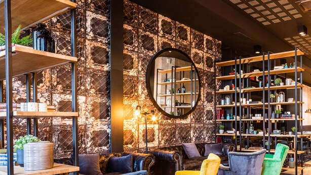 A modern interior with exposed brick walls, wooden shelves, leather seating, and a circular mirror. - ibis Le Mans Centre Gare Nord (Le Mans)