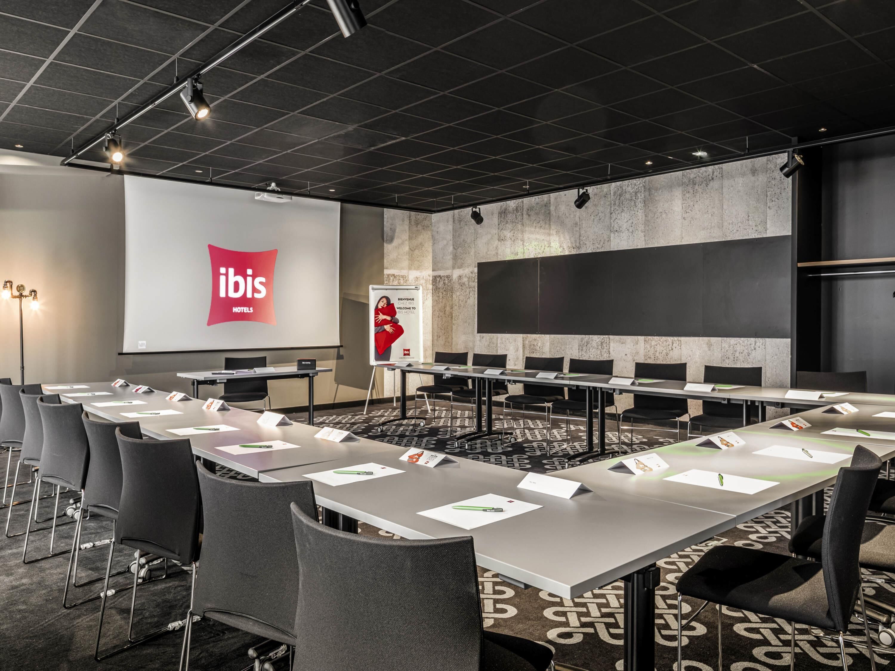 A conference room with a long table, chairs, a projector screen, and a presentation board.