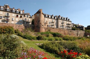 Un edificio de piedra histórico con una torre, rodeado de jardines cuidados y un cielo despejado.