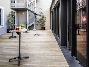 A modern hotel courtyard with a spiral staircase, outdoor seating with food, and potted plants. - ibis Le Mans Centre Gare Nord (Le Mans)