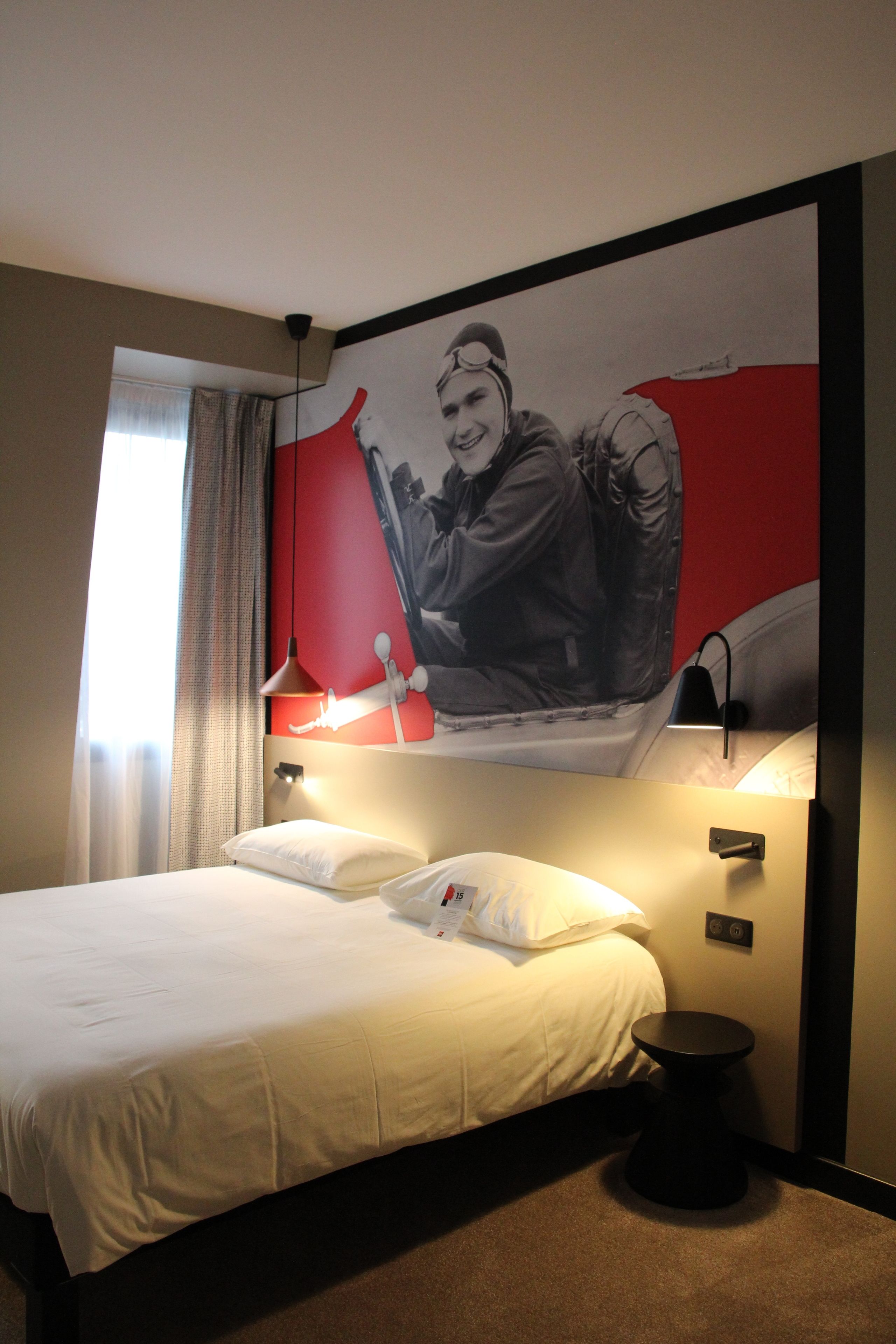 A hotel room with a bed, a nightstand, a lamp, and a large poster on the wall.