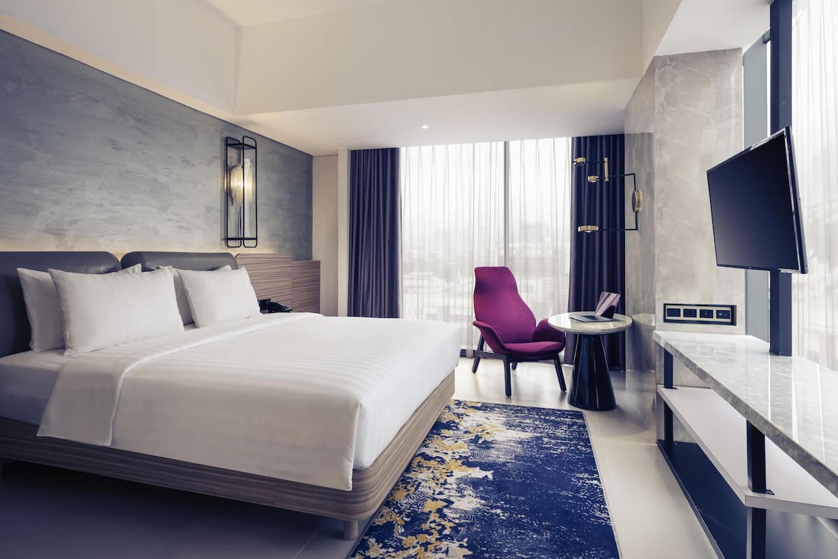 Ein modernes Hotelzimmer mit einem großen Bett, einem Schreibtisch, einem Sessel und einem Fernseher.