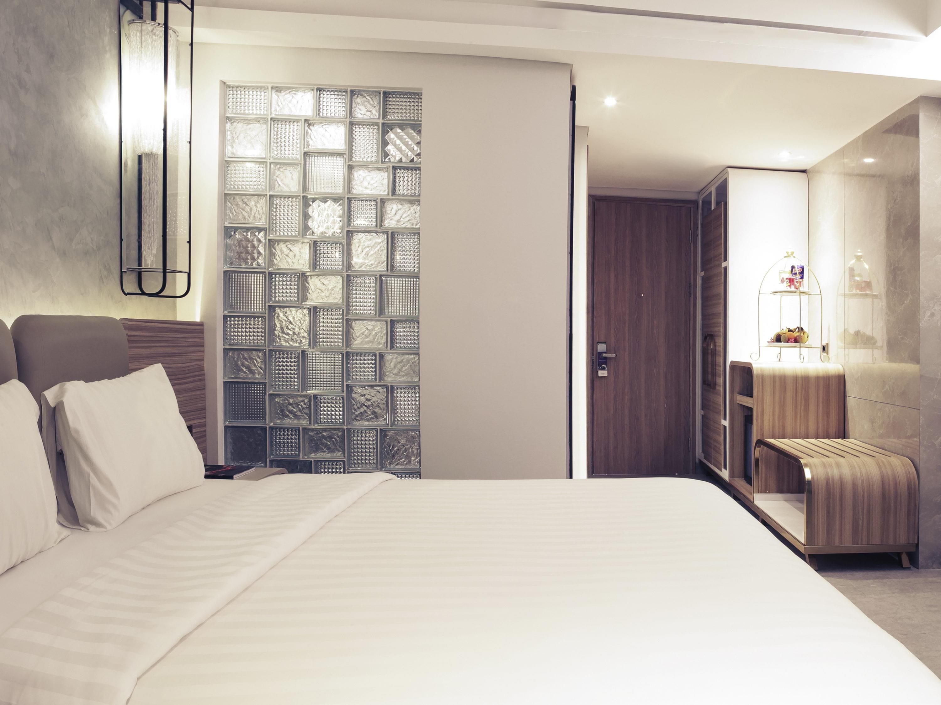 Una habitación de hotel moderna con una cama grande, un armario, un espejo y un panel decorativo en la pared.