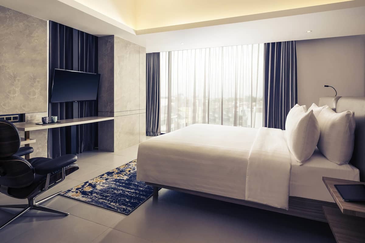 Une chambre d’hôtel moderne équipée d’un lit, d’un bureau avec une chaise, d’une télévision et offrant une vue sur la ville.