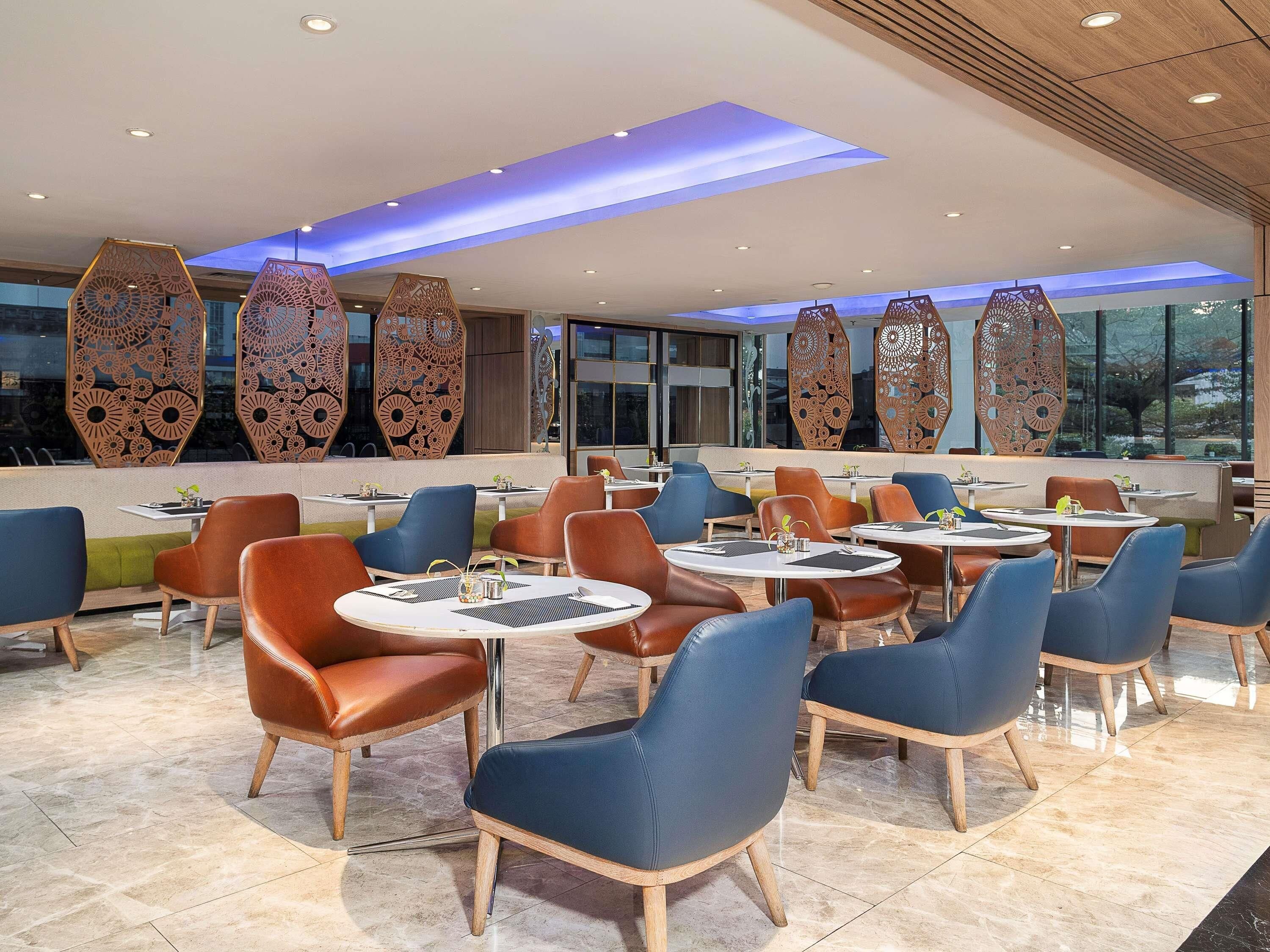 Un restaurante moderno con mesas y sillas redondas, paneles decorativos en la pared y vistas amplias a través de grandes ventanales.