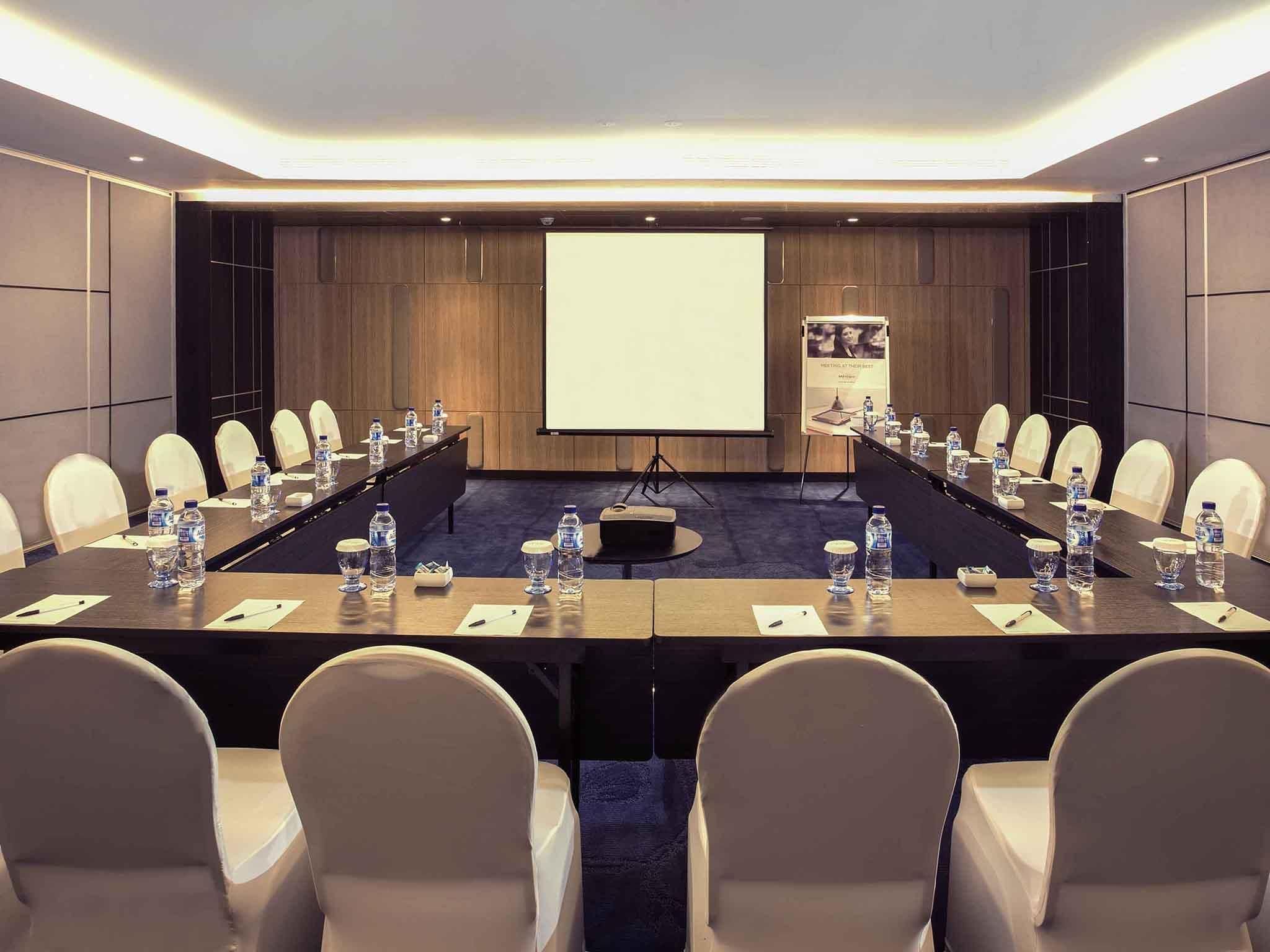 A conference room with a long table, chairs, a projector screen, and water bottles.