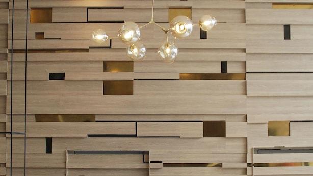 Ein modernes Interieur mit einem geometrischen Wanddesign, einer hängenden Leuchte und drei schwarzen Stühlen.