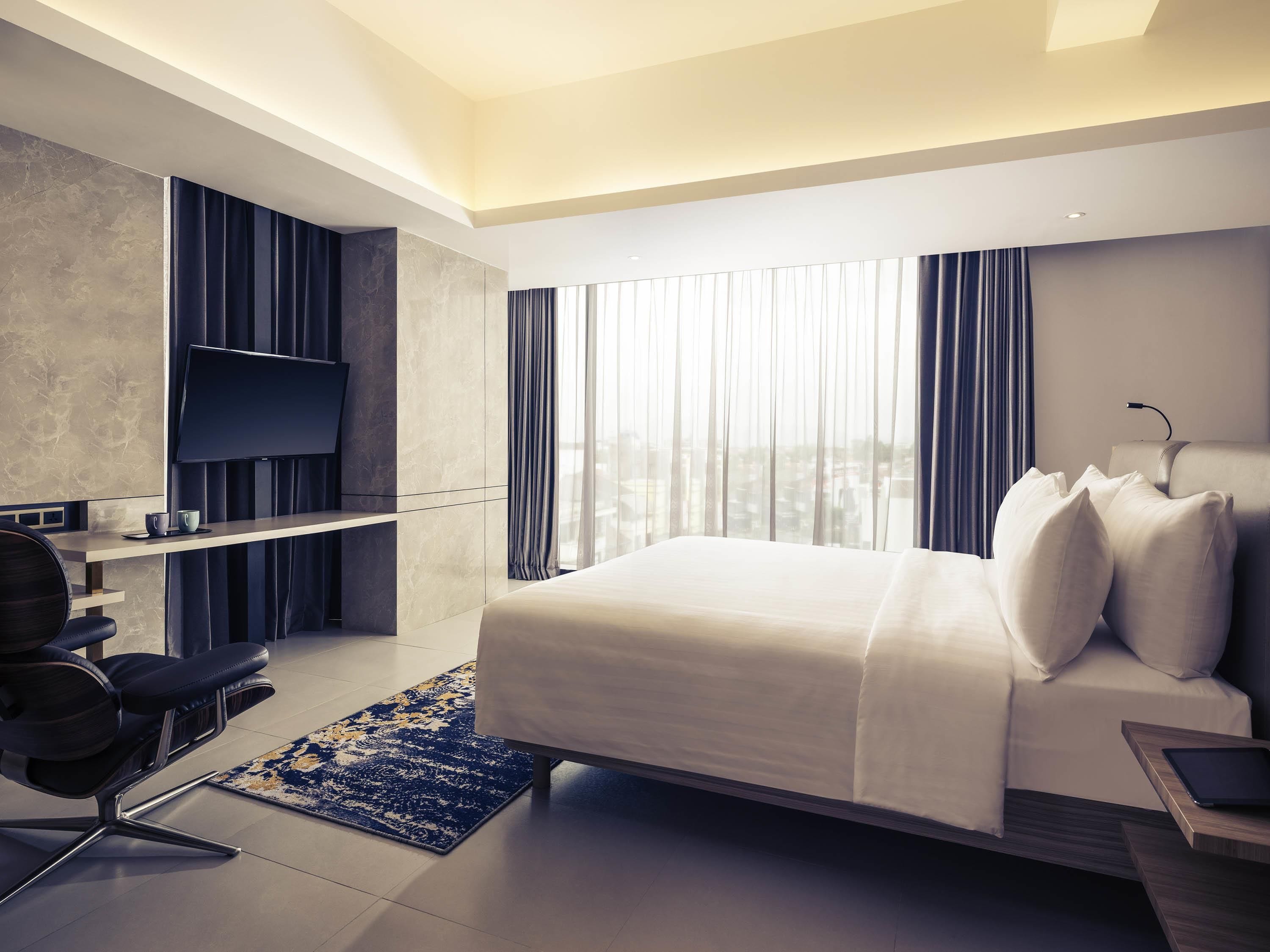 Habitación de hotel moderna con cama, escritorio, silla, televisor y vista a la ciudad.