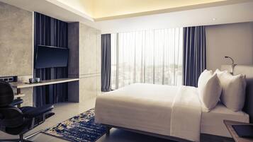 Habitación de hotel moderna con cama, escritorio, silla, televisor y vista a la ciudad.