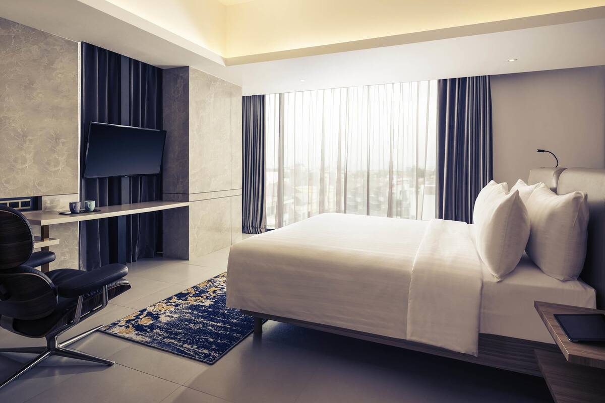 Une chambre d’hôtel moderne équipée d’un lit, d’un bureau, d’une chaise, d’une télévision et offrant une vue sur la ville.