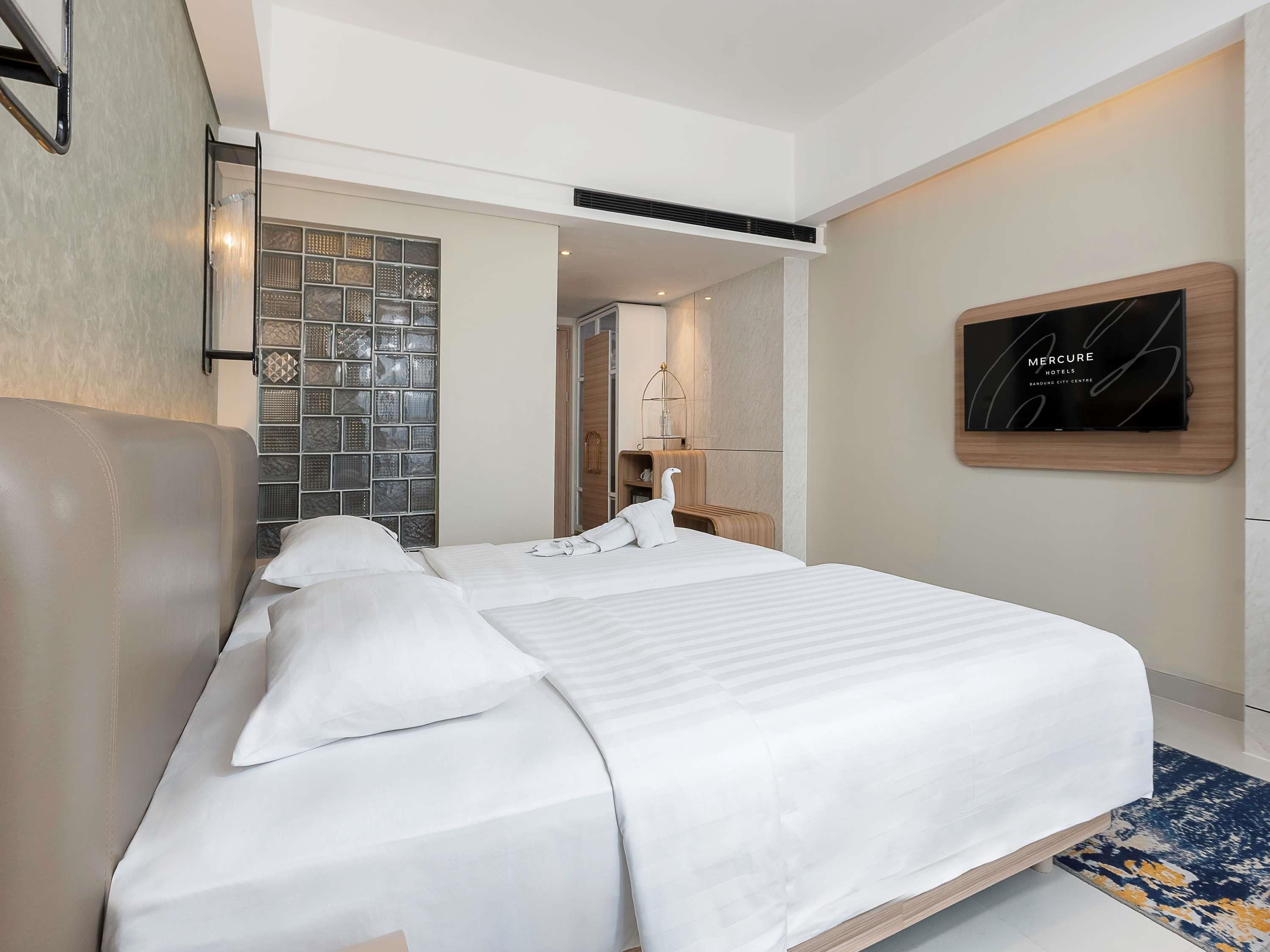 A modern hotel room with a large bed, a TV mounted on the wall, and a decorative wall panel.