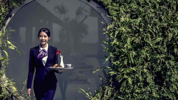 Una persona con traje oscuro lleva una bandeja con una flor, una taza y un pastel.