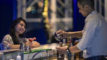 A bartender preparing a drink at a bar with a woman seated behind him.