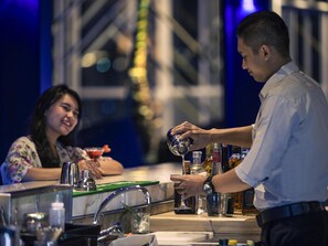 A bartender preparing a drink at a bar with a woman seated behind him. - Mercure Bandung City Centre (Bandung)