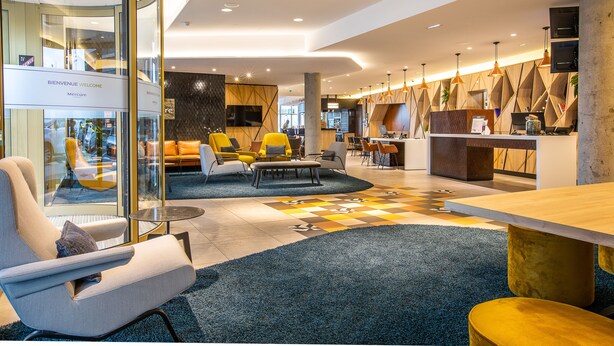 Een moderne lobby met een receptiebalie, een zithoek en een incheckbalie.