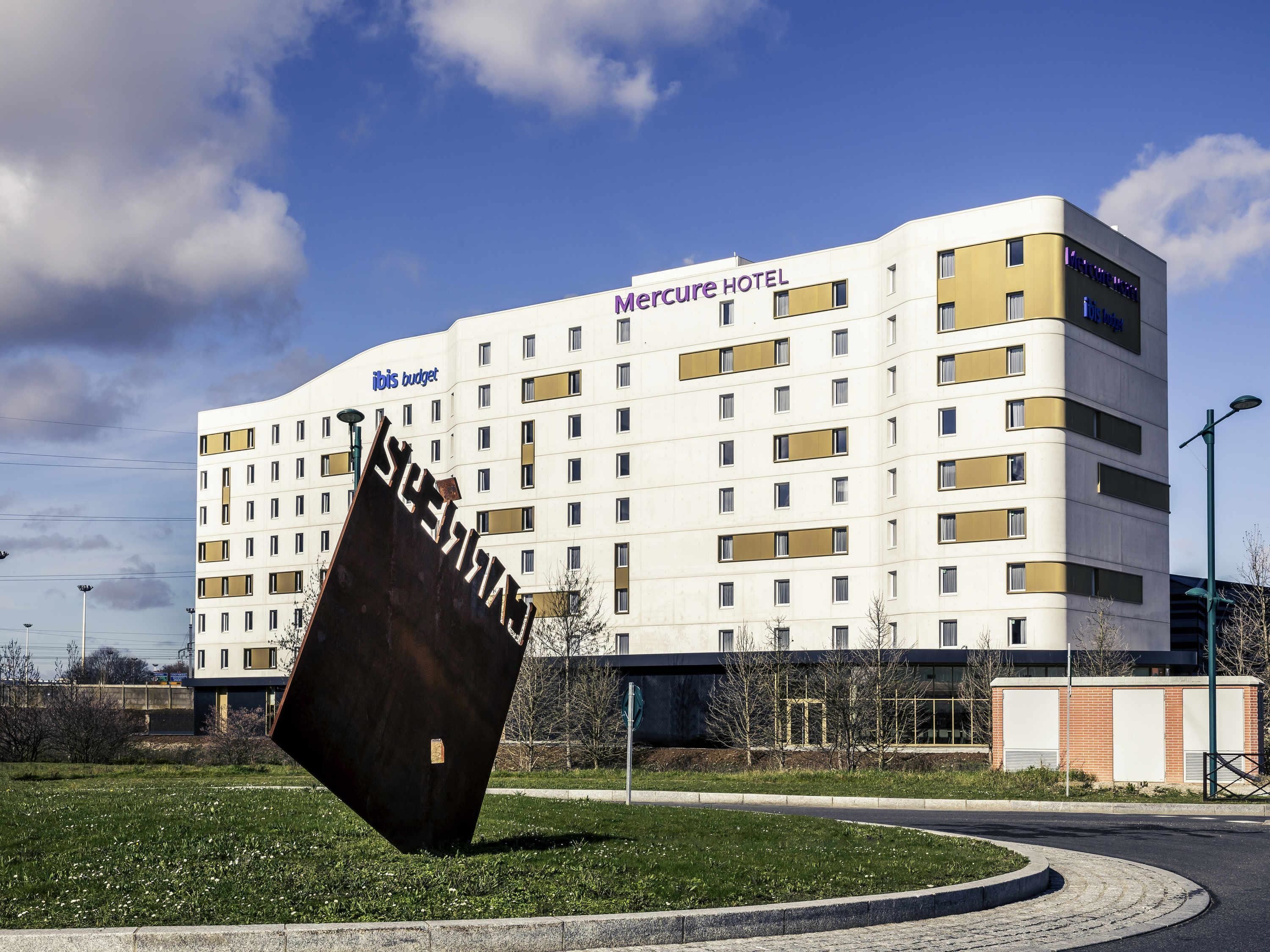 Un hôtel Mercure au design moderne, avec une grande sculpture devant l’entrée.