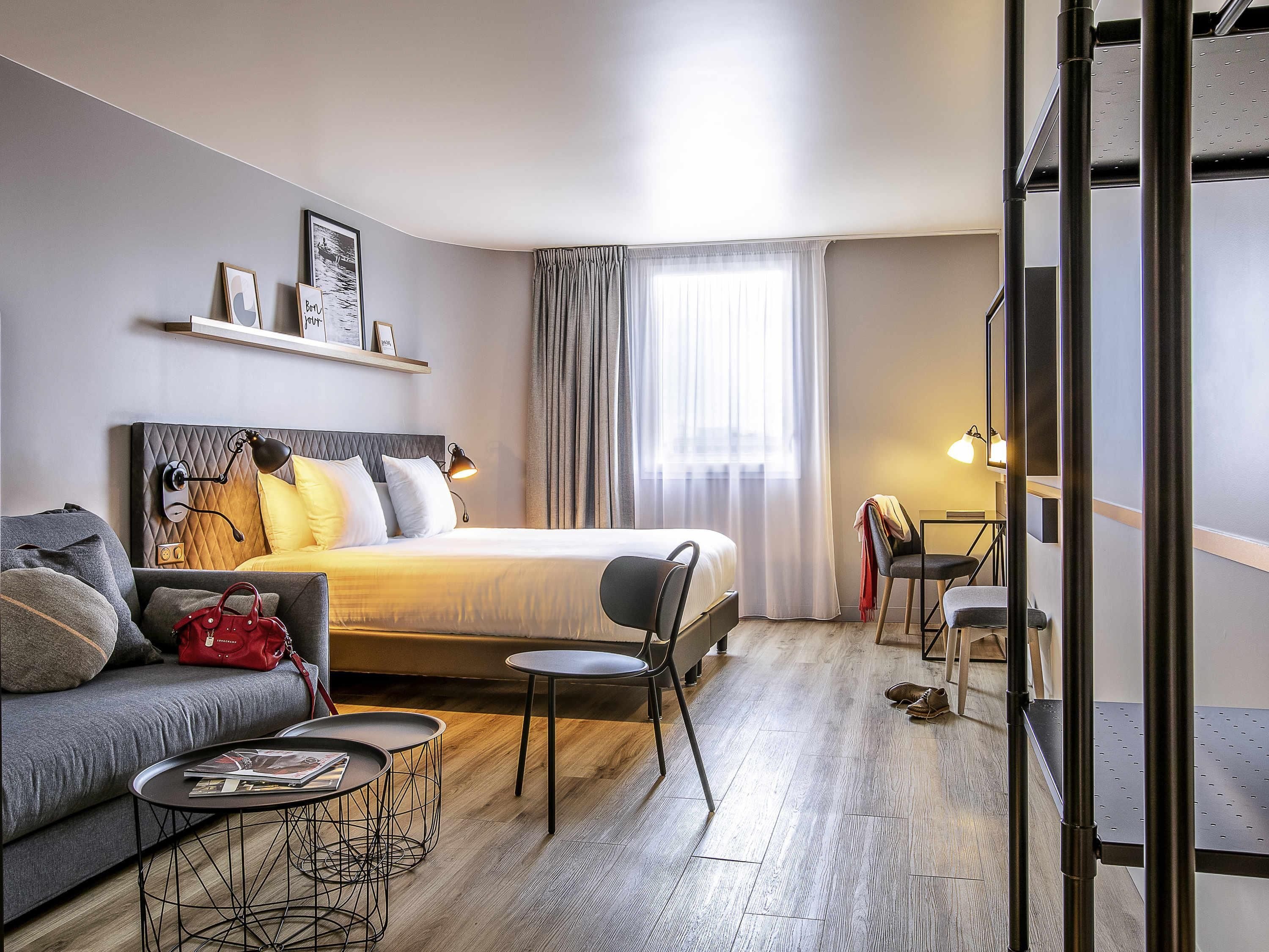 A modern hotel room with a bed, a sofa, a small table, and a chair.