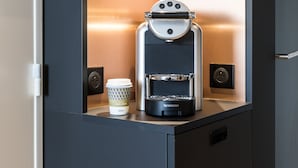 Een compact, modern kitchenette met een ingebouwde espressomachine, een koffiekop en een klein kastje.