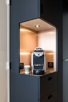 Una kitchenette compacta y moderna con una cafetera espresso integrada, una taza de café y un mueble pequeño.