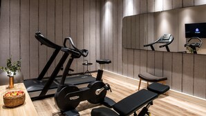 Een sportschool met fitnessapparatuur, een bank, een spiegel en een tv aan de muur.